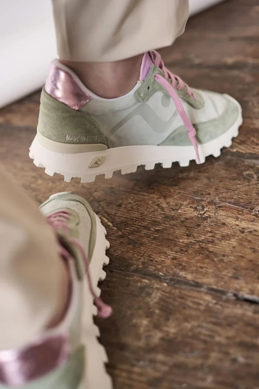 Detailopname van trendy groen-roze designer sneakers op een houten vloer.
